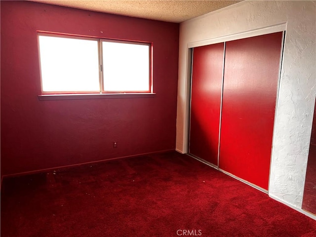 unfurnished bedroom featuring a textured ceiling, a textured wall, a closet, and carpet flooring