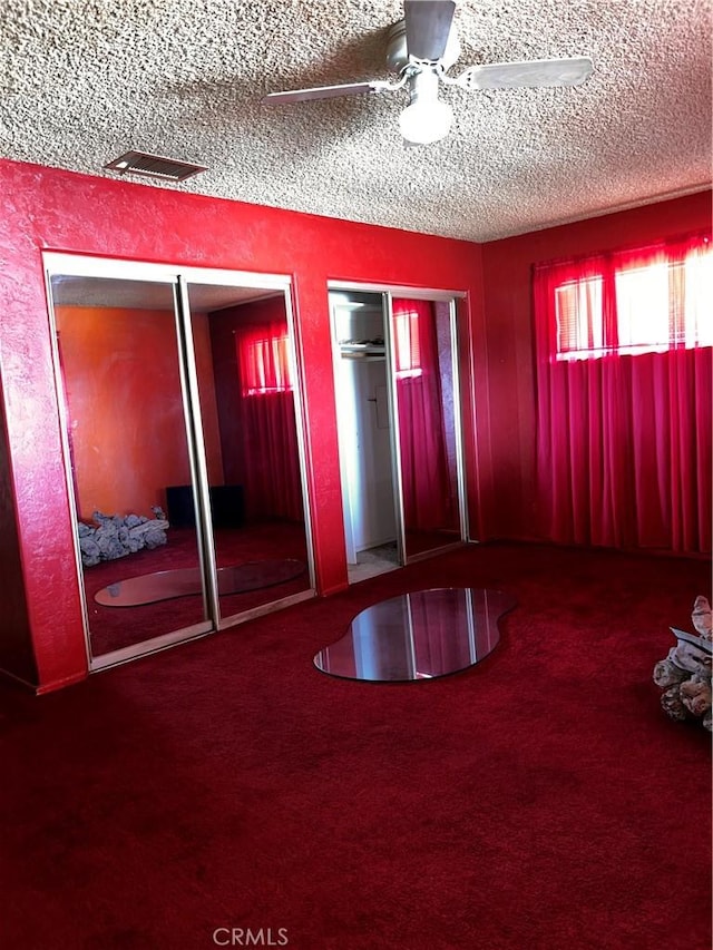 unfurnished bedroom featuring a textured ceiling, ceiling fan, visible vents, multiple closets, and carpet