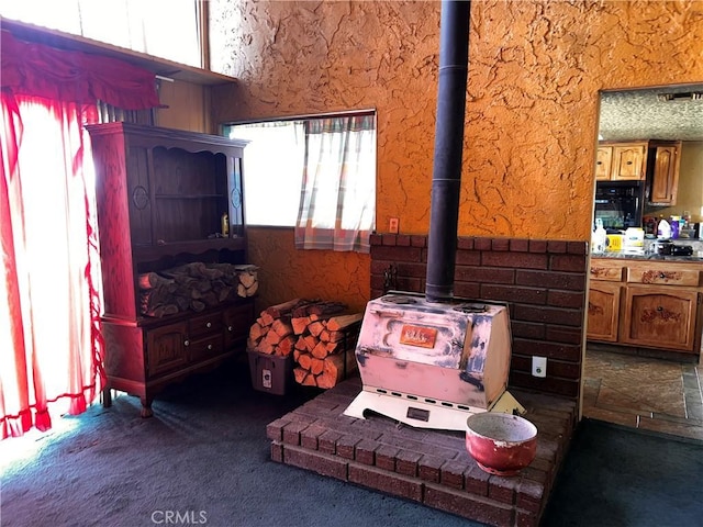 living room featuring a wood stove, plenty of natural light, and dark carpet