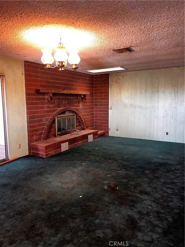 unfurnished living room featuring carpet, a fireplace, a textured ceiling, and an inviting chandelier