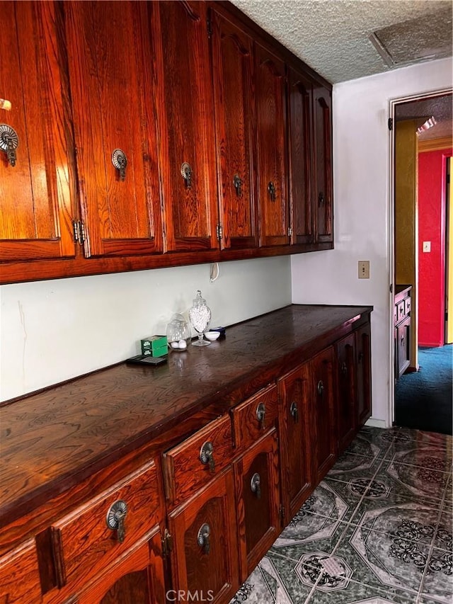 interior space featuring a textured ceiling, dark countertops, and reddish brown cabinets