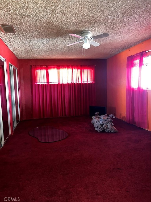 carpeted empty room featuring a ceiling fan, a wealth of natural light, visible vents, and a textured ceiling