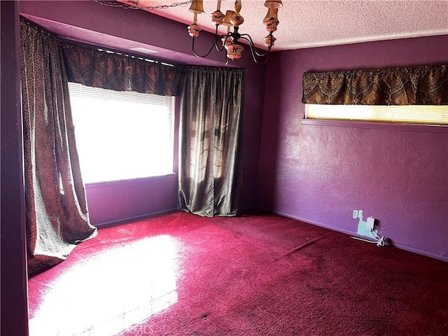 empty room with a textured ceiling, a textured wall, carpet, and a notable chandelier