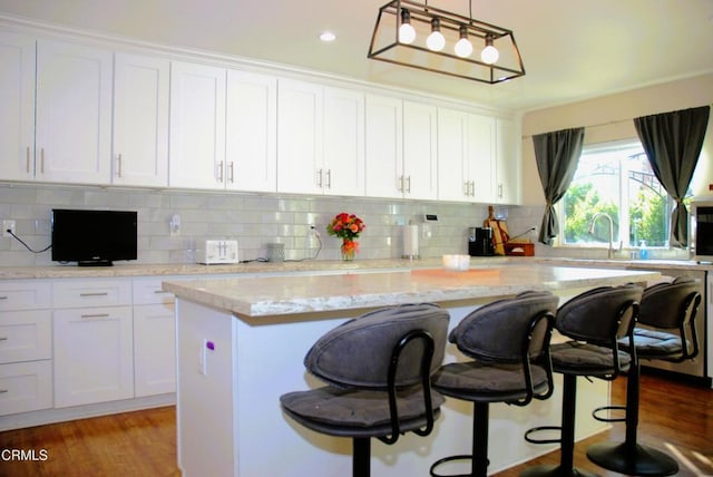 kitchen featuring pendant lighting, a kitchen bar, a center island, and white cabinets