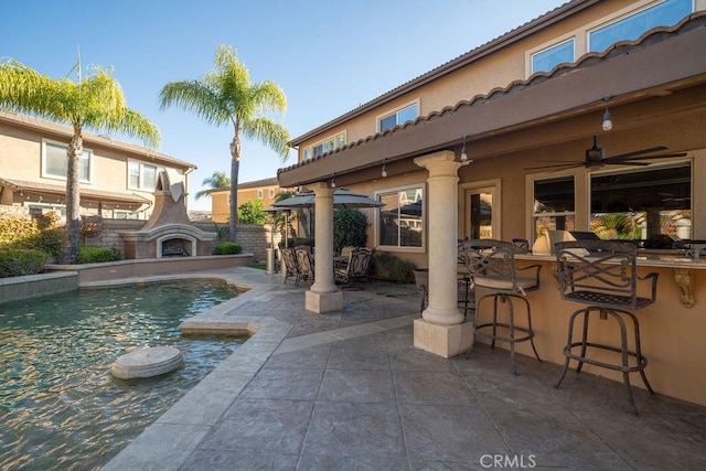 view of swimming pool with exterior fireplace, ceiling fan, a patio, and exterior bar