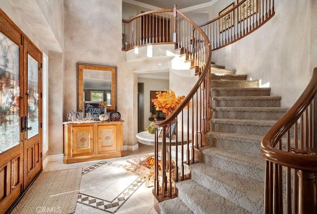 foyer featuring a high ceiling, light tile patterned floors, crown molding, and french doors