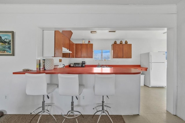 kitchen with a breakfast bar area, kitchen peninsula, and white fridge