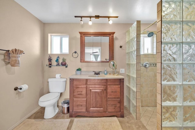 bathroom featuring toilet, a tile shower, rail lighting, tile patterned floors, and vanity