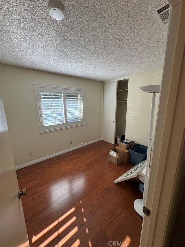 unfurnished bedroom featuring dark wood-type flooring, a closet, and a textured ceiling