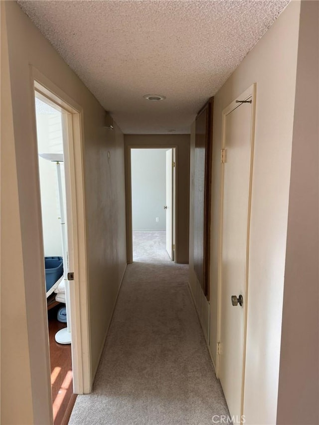 hallway featuring light carpet and a textured ceiling