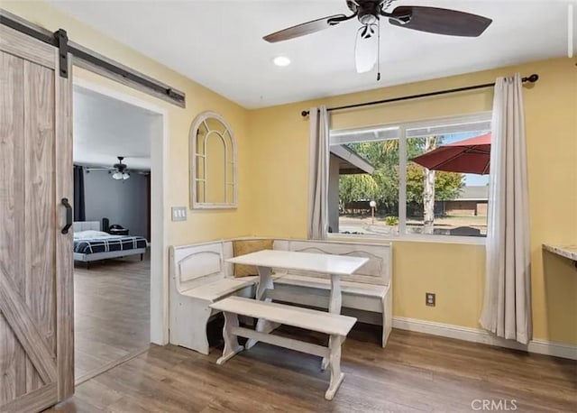 dining space with ceiling fan, a barn door, and hardwood / wood-style flooring