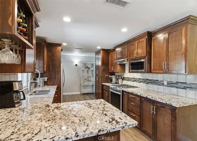 kitchen featuring stainless steel appliances, tasteful backsplash, light wood-type flooring, light stone countertops, and sink