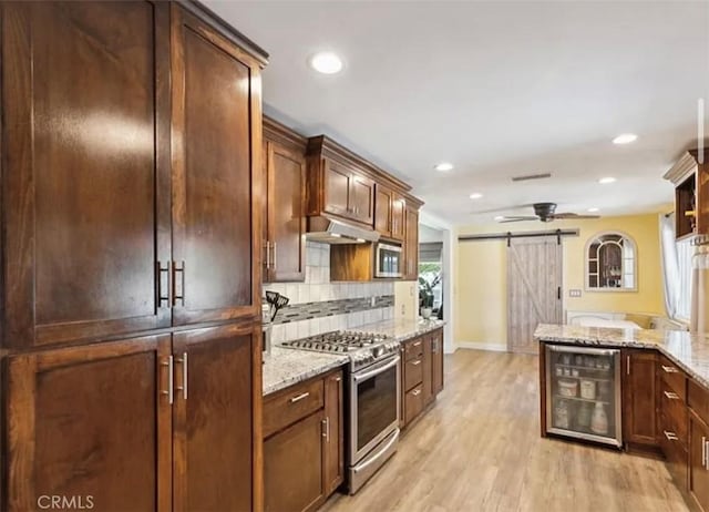 kitchen featuring a barn door, light hardwood / wood-style flooring, light stone countertops, stainless steel appliances, and beverage cooler