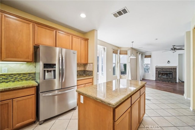 kitchen featuring stainless steel fridge with ice dispenser, a center island, light tile patterned floors, and a brick fireplace