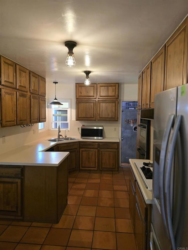 kitchen featuring appliances with stainless steel finishes, dark tile patterned floors, sink, hanging light fixtures, and kitchen peninsula