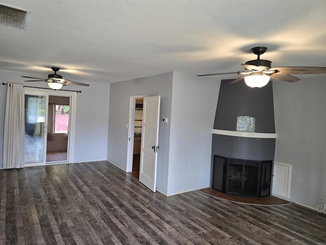 unfurnished living room with dark wood-type flooring, a large fireplace, and ceiling fan