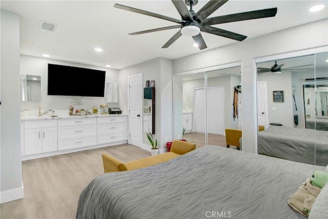 bedroom with ceiling fan, ensuite bathroom, two closets, and light hardwood / wood-style flooring