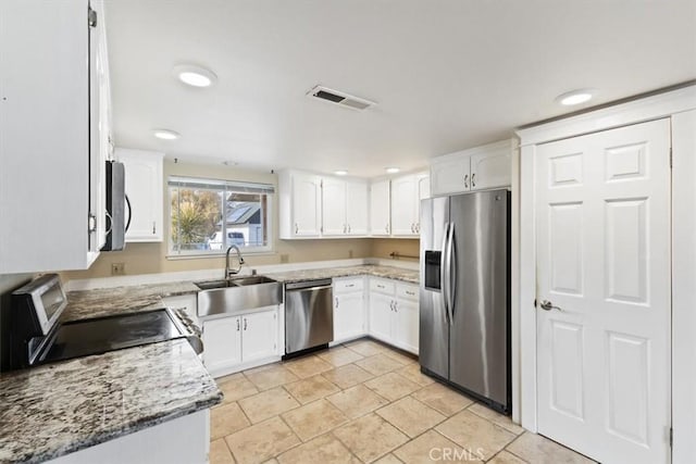 kitchen with appliances with stainless steel finishes, light tile patterned flooring, white cabinets, light stone counters, and sink