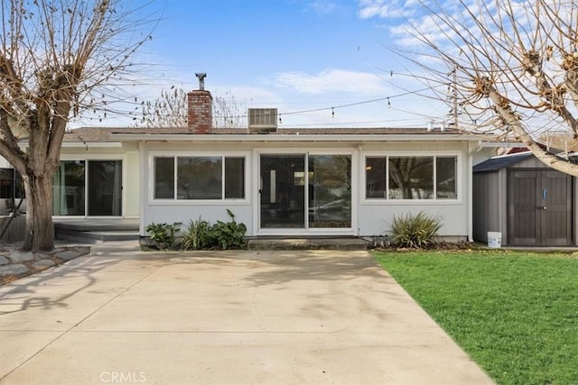 rear view of property featuring cooling unit, a yard, a storage unit, and a patio