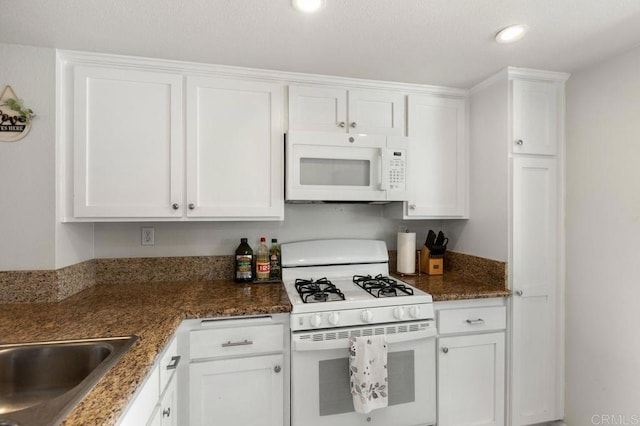 kitchen featuring white cabinets, dark stone counters, and white appliances