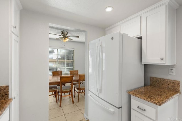 kitchen featuring white fridge, light tile patterned floors, ceiling fan, dark stone counters, and white cabinets