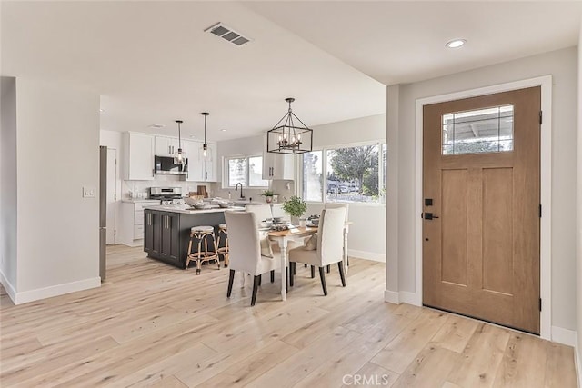 dining space featuring sink, light wood-type flooring, and a notable chandelier