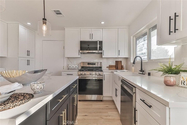 kitchen with light stone counters, stainless steel appliances, sink, white cabinetry, and hanging light fixtures