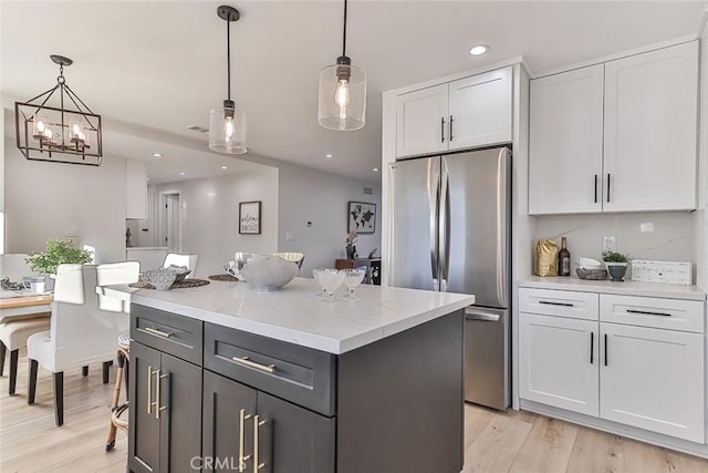 kitchen with stainless steel refrigerator, white cabinetry, a kitchen island, and decorative light fixtures