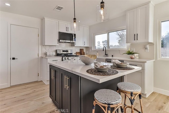 kitchen with decorative light fixtures, a center island, white cabinetry, and stainless steel appliances