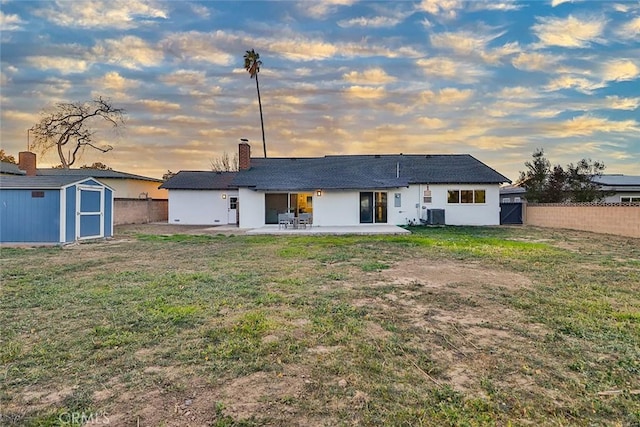 back house at dusk with a yard, a shed, a patio area, and central air condition unit