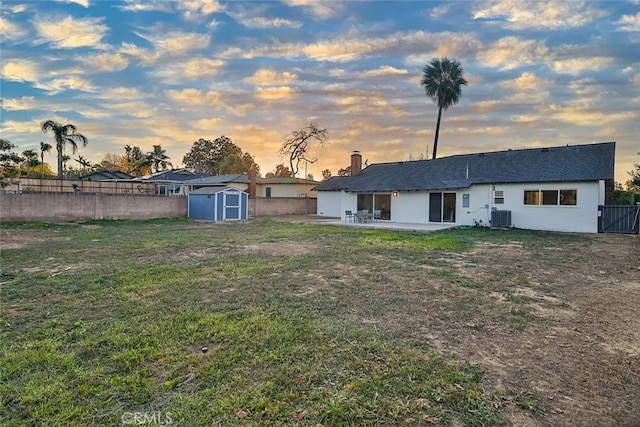 yard at dusk featuring a shed, central AC unit, and a patio area