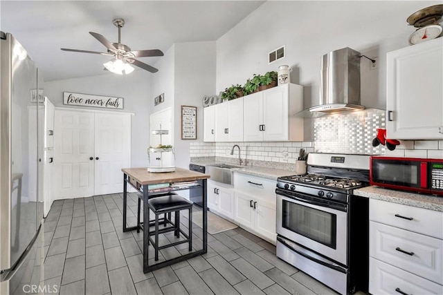 kitchen featuring vaulted ceiling, sink, white cabinets, wall chimney exhaust hood, and gas range