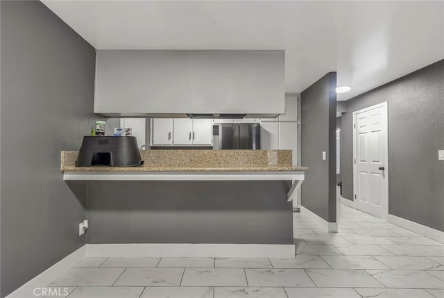 kitchen featuring a breakfast bar area, kitchen peninsula, refrigerator, and white cabinetry