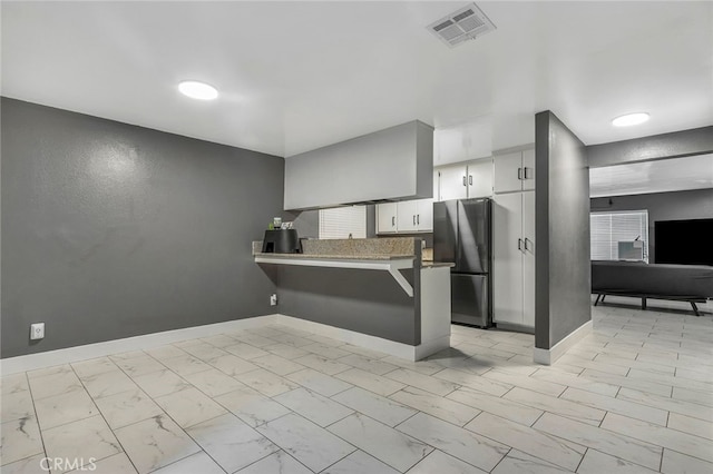 kitchen with kitchen peninsula, decorative backsplash, white cabinets, and fridge