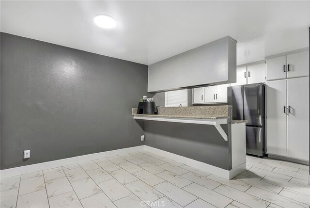 kitchen featuring white cabinetry, kitchen peninsula, and stainless steel refrigerator