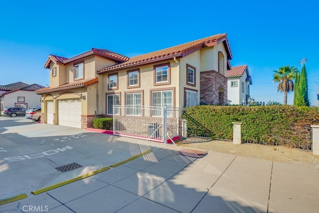 mediterranean / spanish home featuring a garage, a tile roof, stone siding, driveway, and stucco siding