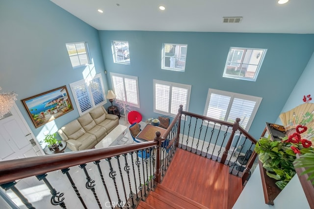 stairway featuring recessed lighting, visible vents, a high ceiling, and wood finished floors