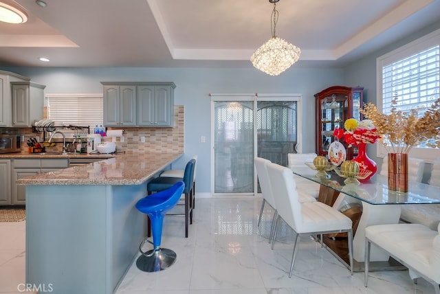 kitchen with gray cabinetry, a raised ceiling, and pendant lighting