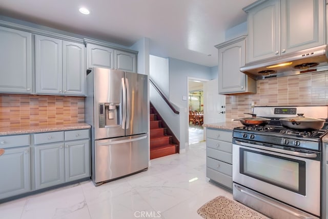 kitchen featuring marble finish floor, tasteful backsplash, appliances with stainless steel finishes, light stone countertops, and under cabinet range hood