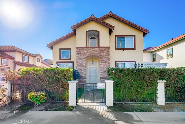 mediterranean / spanish home with a fenced front yard, a gate, stone siding, and stucco siding