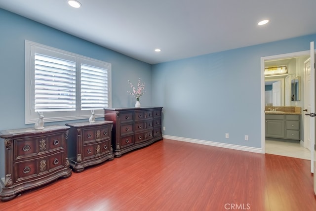 bedroom with light wood finished floors, baseboards, ensuite bath, a sink, and recessed lighting