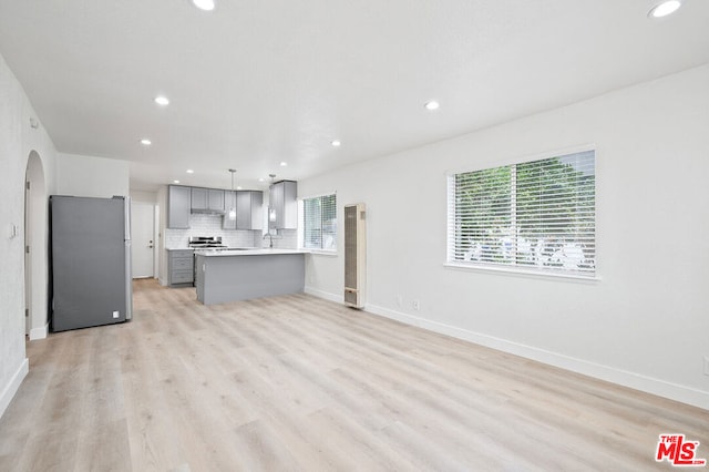 kitchen featuring range, decorative backsplash, gray cabinets, kitchen peninsula, and stainless steel refrigerator