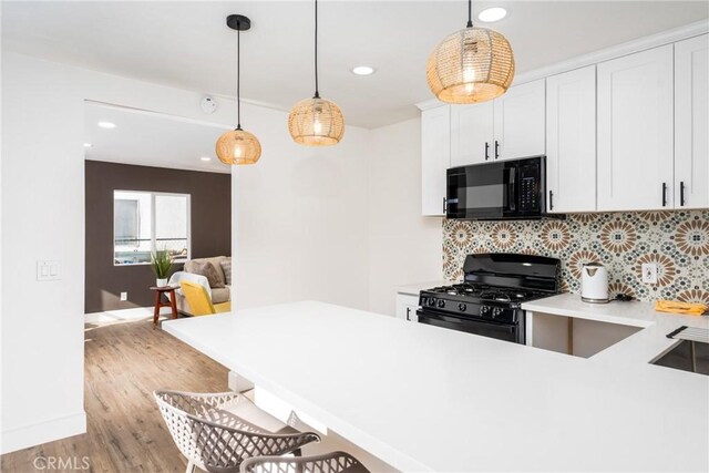 kitchen with white cabinetry, hanging light fixtures, decorative backsplash, black appliances, and light wood-type flooring