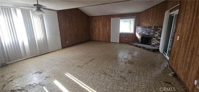 unfurnished living room featuring ceiling fan, a brick fireplace, wood walls, and a textured ceiling