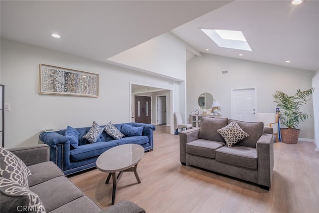 living room with high vaulted ceiling, a skylight, and light hardwood / wood-style flooring