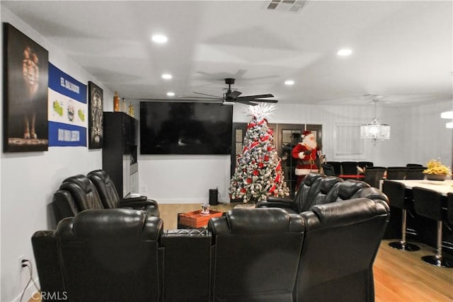 cinema room with ceiling fan with notable chandelier and light wood-type flooring