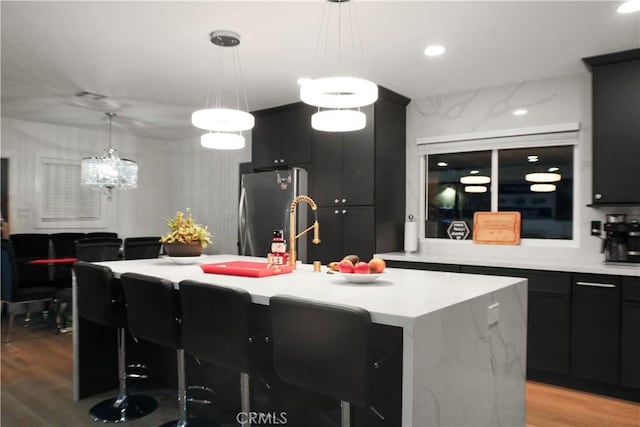 kitchen with hanging light fixtures, a kitchen island with sink, and stainless steel fridge