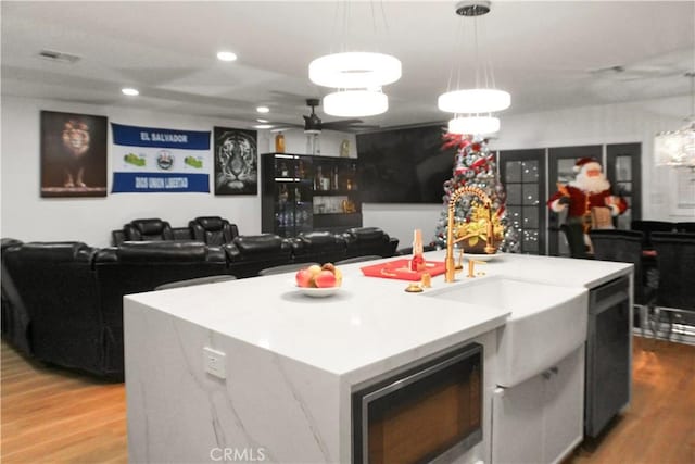 kitchen with light wood-type flooring, a kitchen island with sink, and pendant lighting