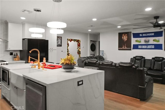 kitchen with white cabinetry, an island with sink, hanging light fixtures, black fridge, and light wood-type flooring