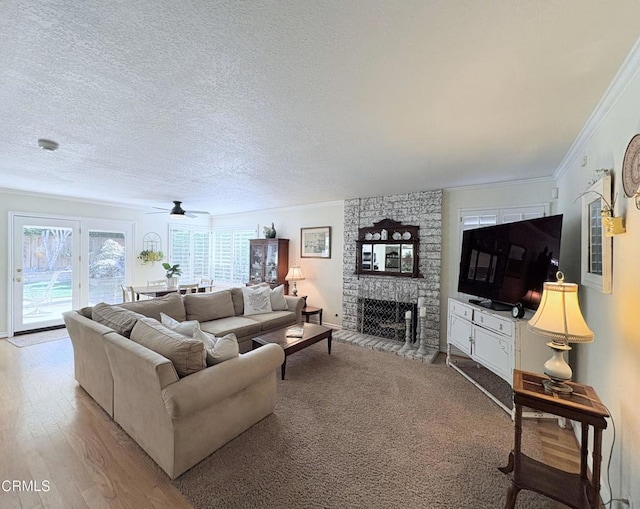 living room with ceiling fan, a brick fireplace, crown molding, light hardwood / wood-style flooring, and a textured ceiling